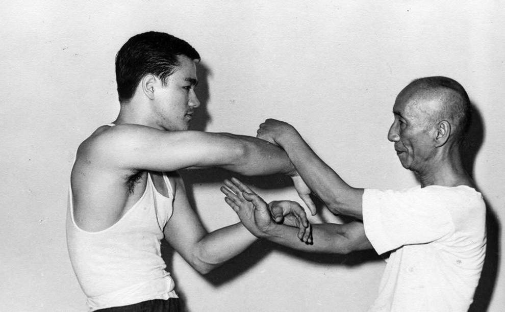 Bruce Lee practising Wing Chun sticky hands with Grandmaster Ip Man. — שילוני, CC BY-SA 4.0 (Wikimedia Commons)